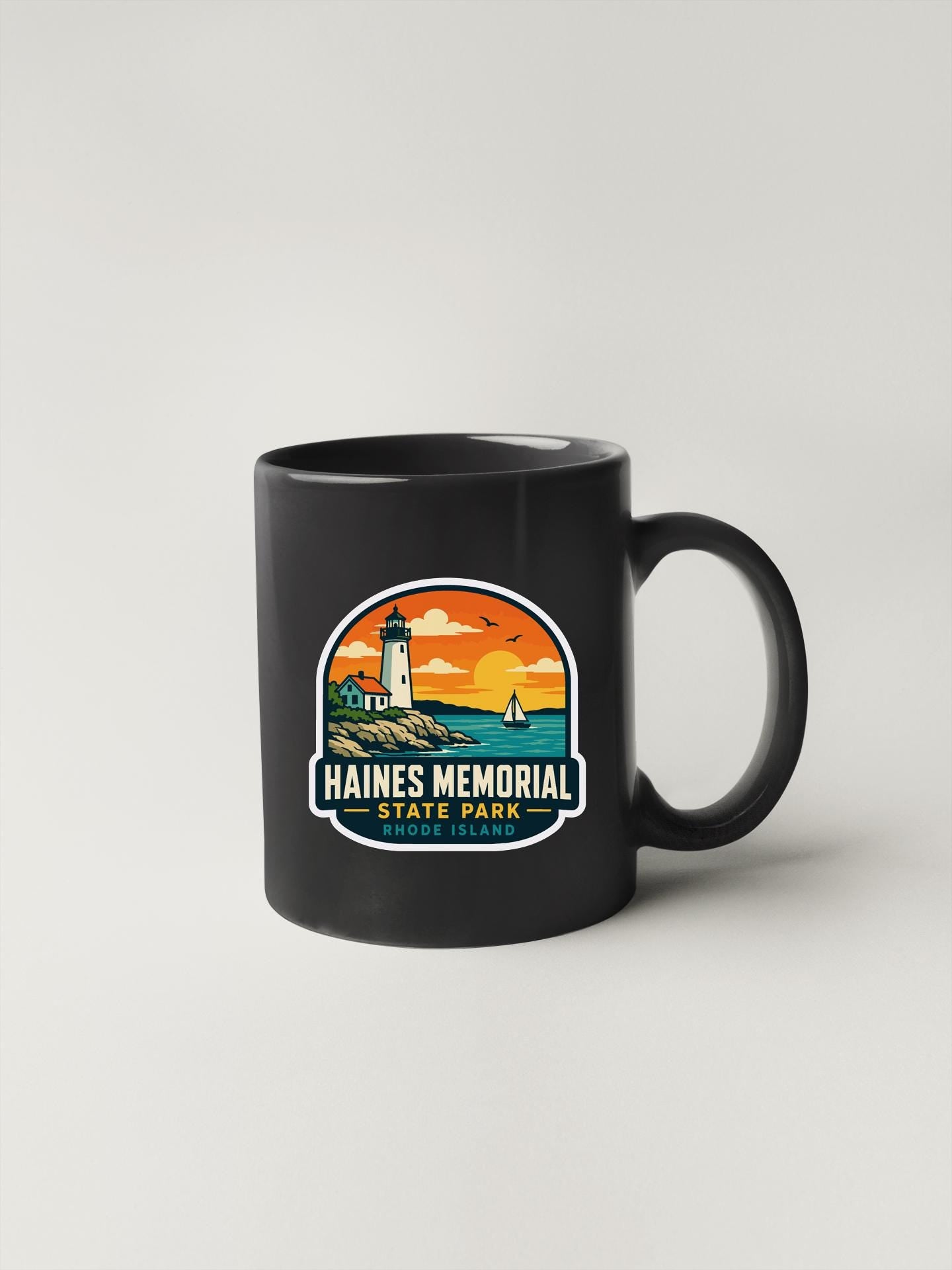 A black coffee mug with a colorful graphic design depicting a lighthouse and a sunset over the ocean.