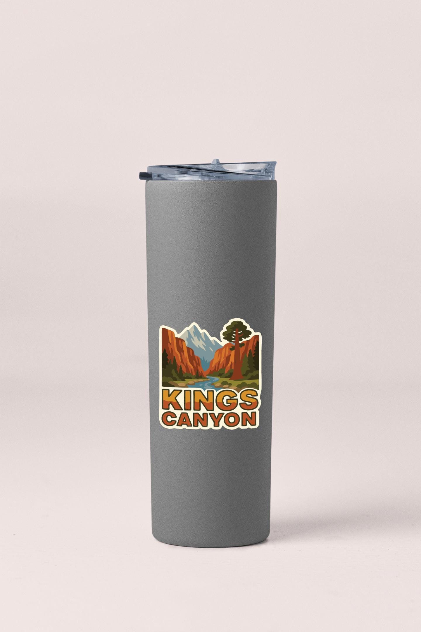 A gray tumbler with a sticker depicting a scenic landscape of mountains and a tree.