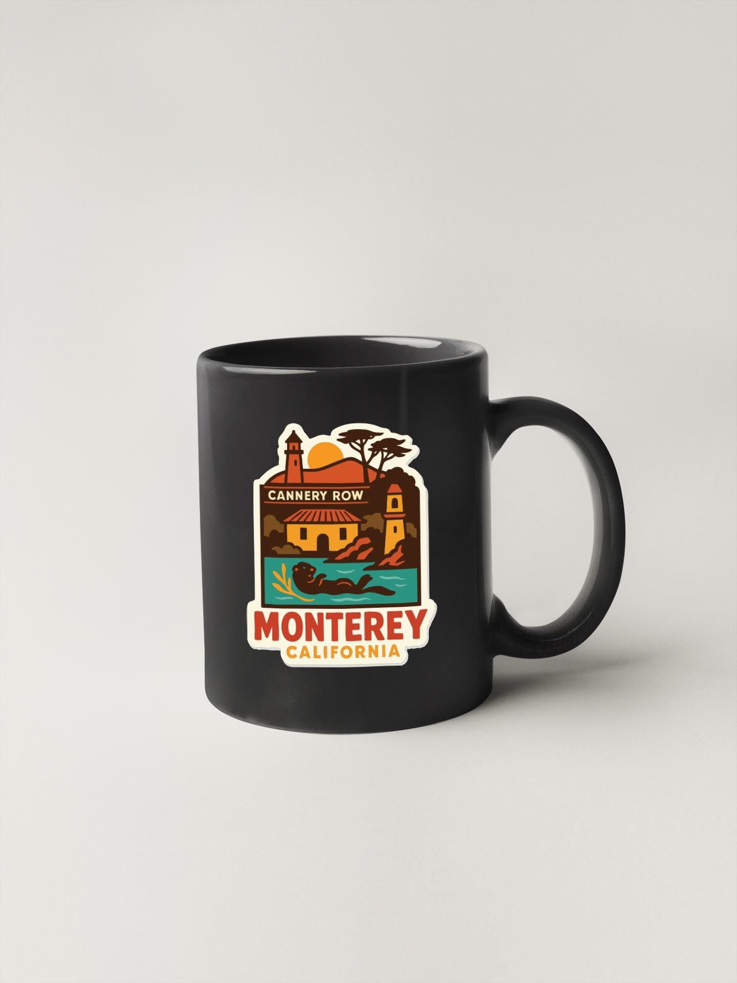 A black coffee mug with a colorful graphic depicting a scenic view of Monterey, California.