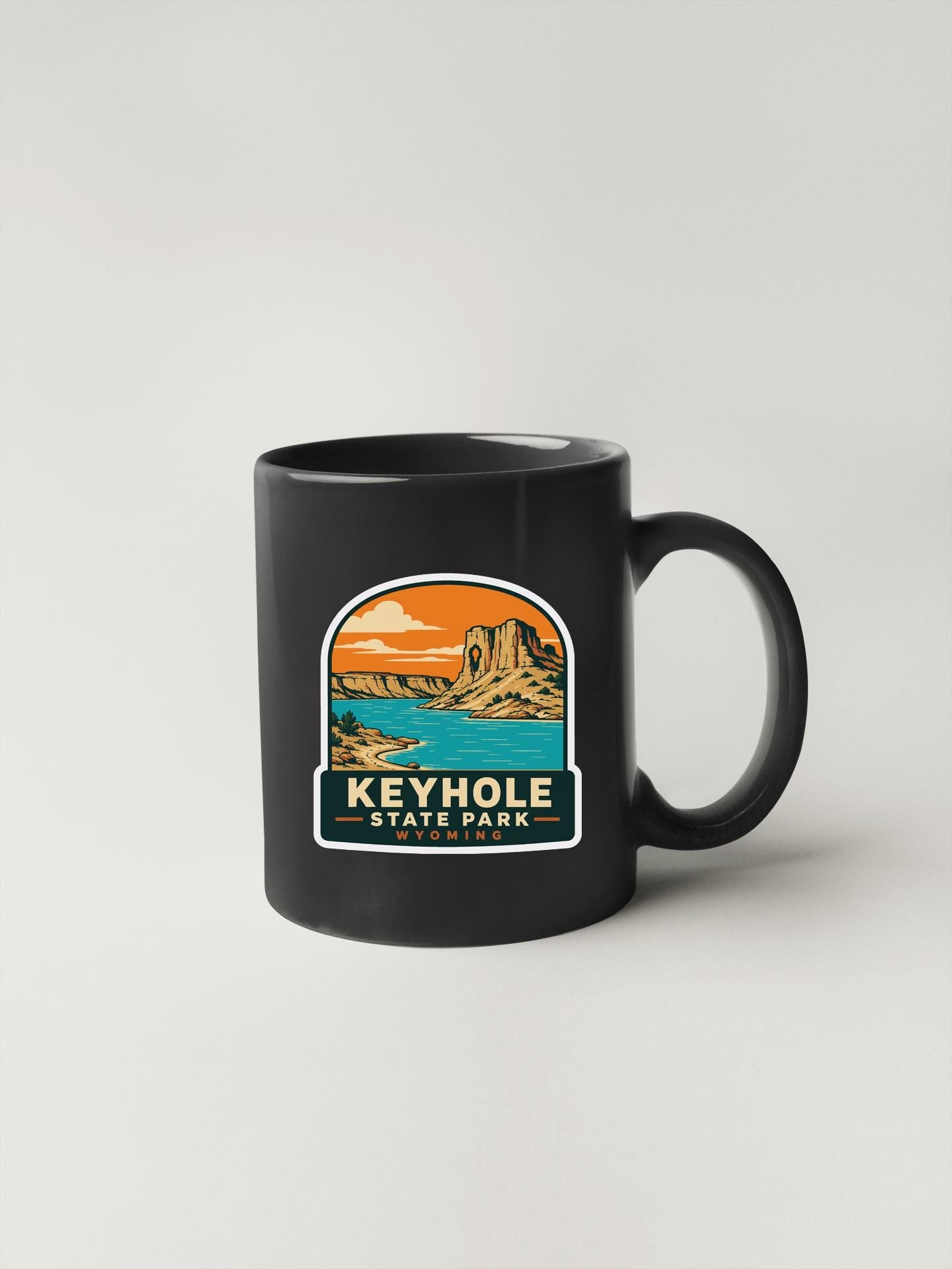 A black coffee mug with a graphic design depicting a scenic landscape, including a mountain, lake, and sky.