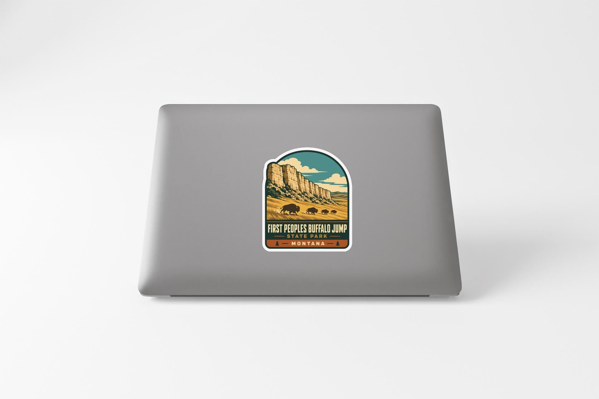 A sticker on the back of a laptop, depicting a scenic landscape with mountains and a buffalo jumping in the distance.