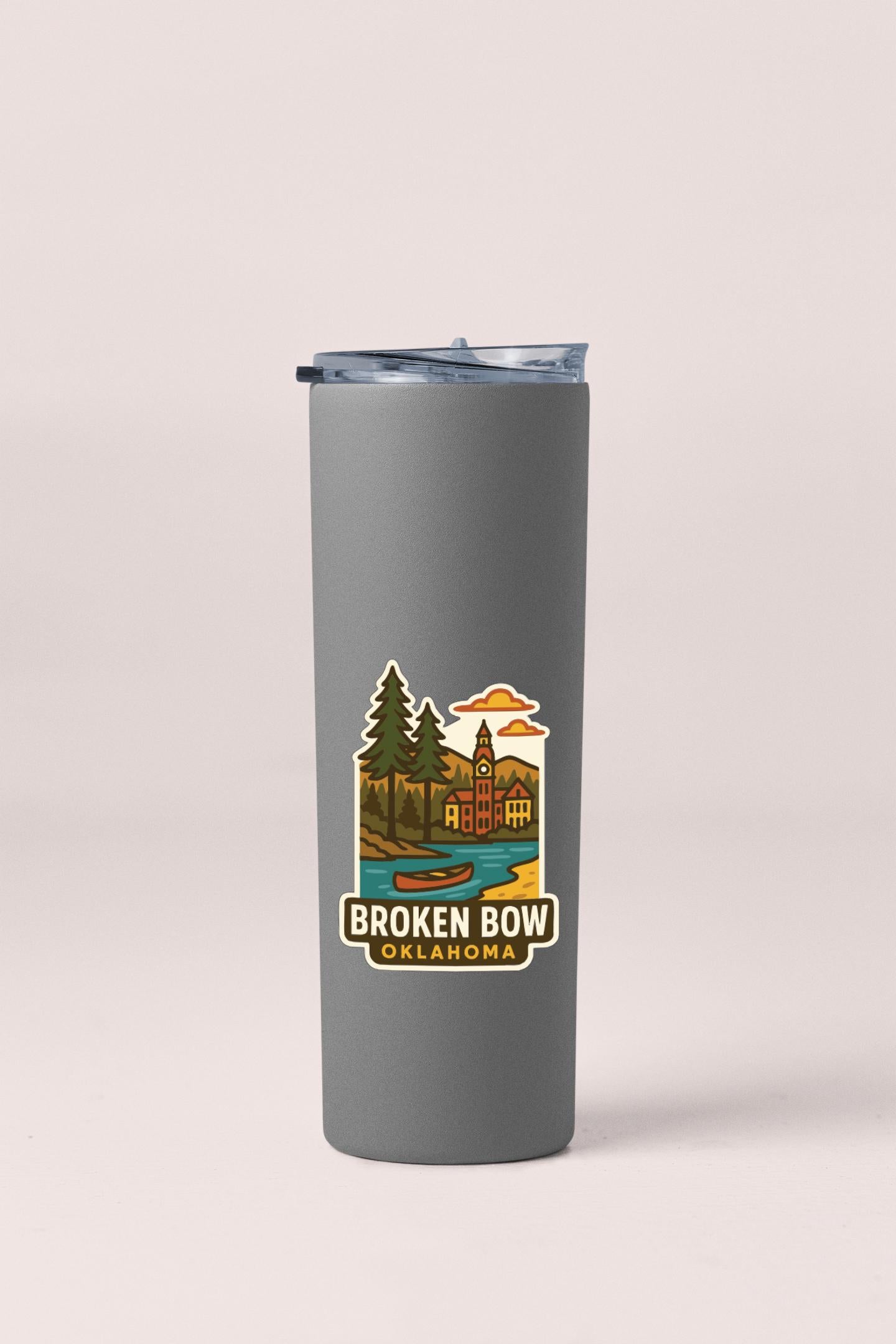 A gray insulated tumbler with a printed label that features a scenic illustration of Broken Bow, Oklahoma.