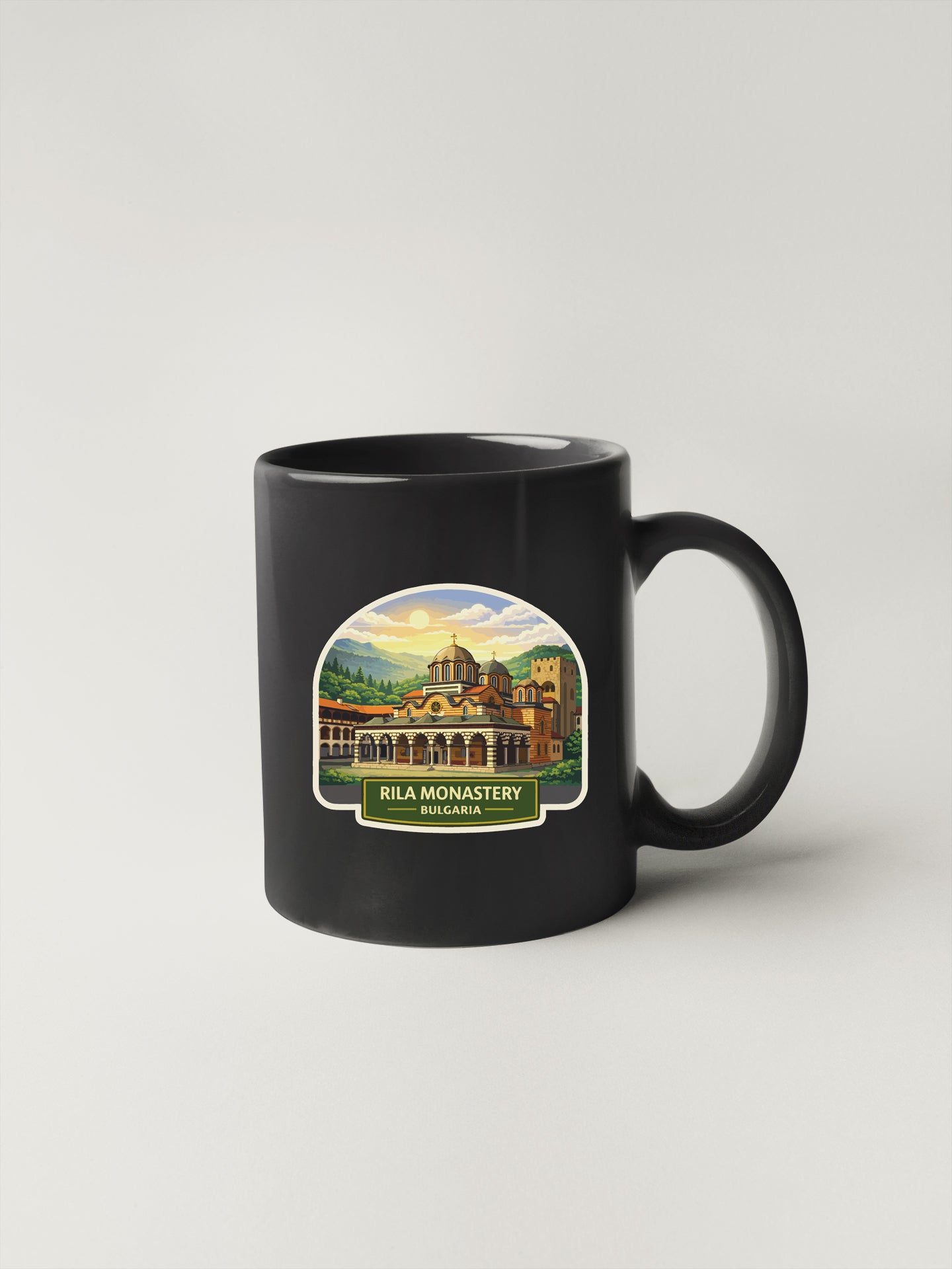 A black coffee mug with a sticker depicting the Rila Monastery in Bulgaria.