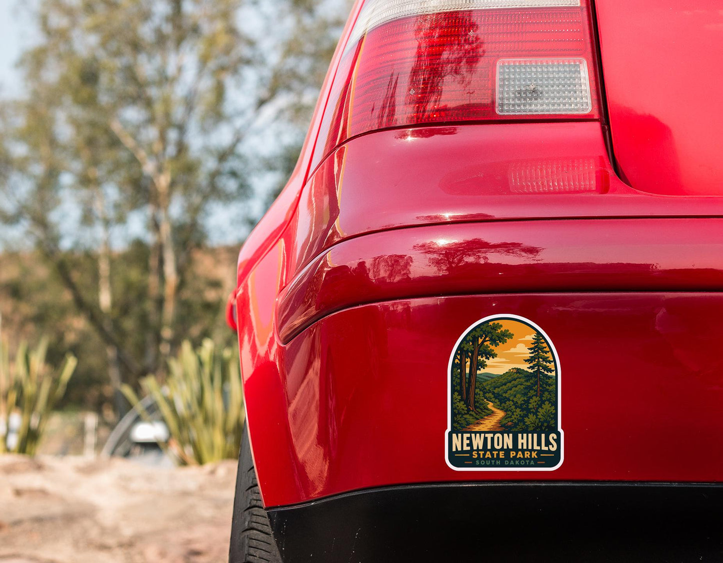 the rear end of a red car with a sticker on the trunk that says "Newton Hills South Dakota".