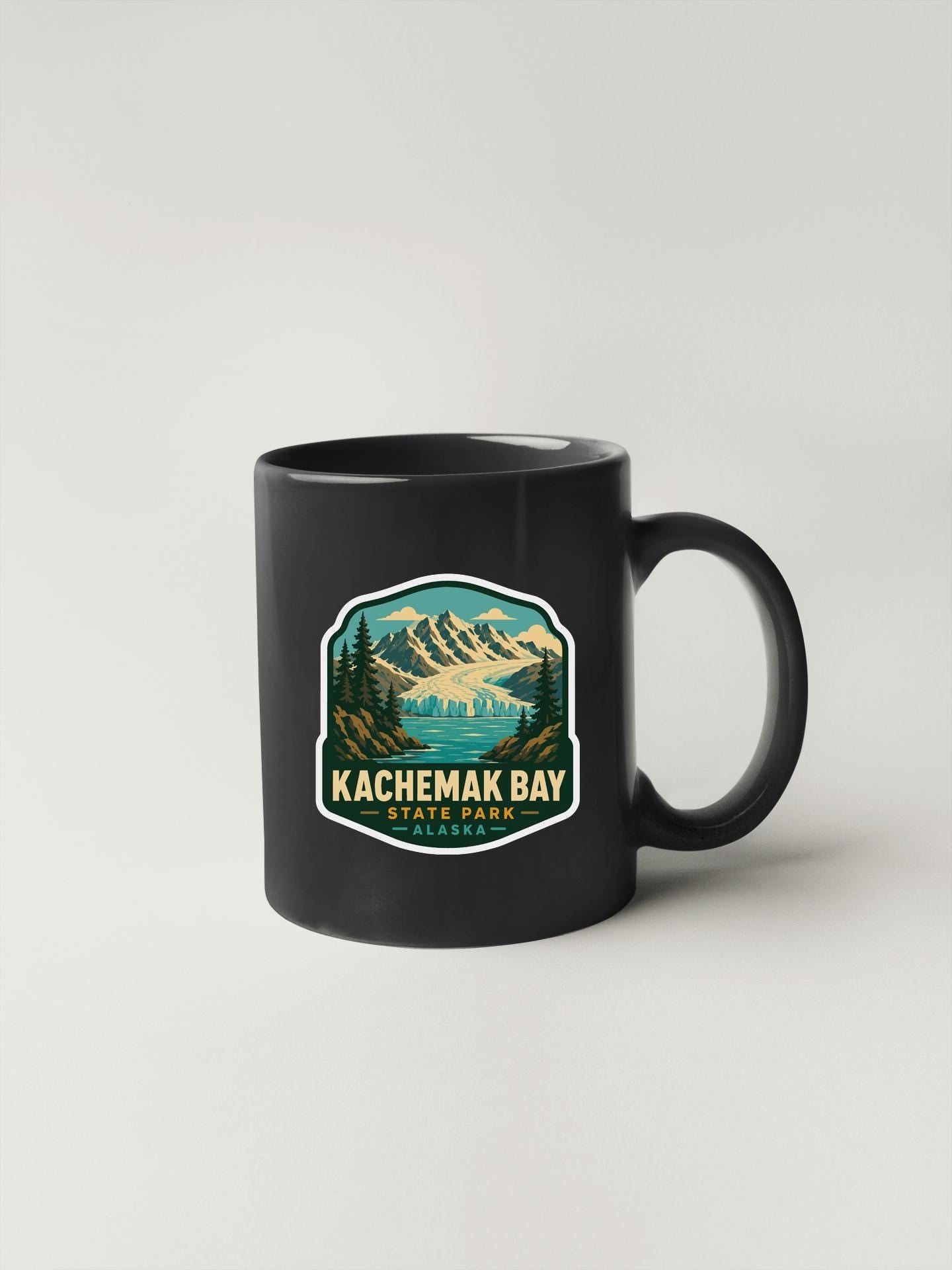 A black coffee mug with a sticker depicting a scenic landscape featuring mountains, pine trees, and a lake.