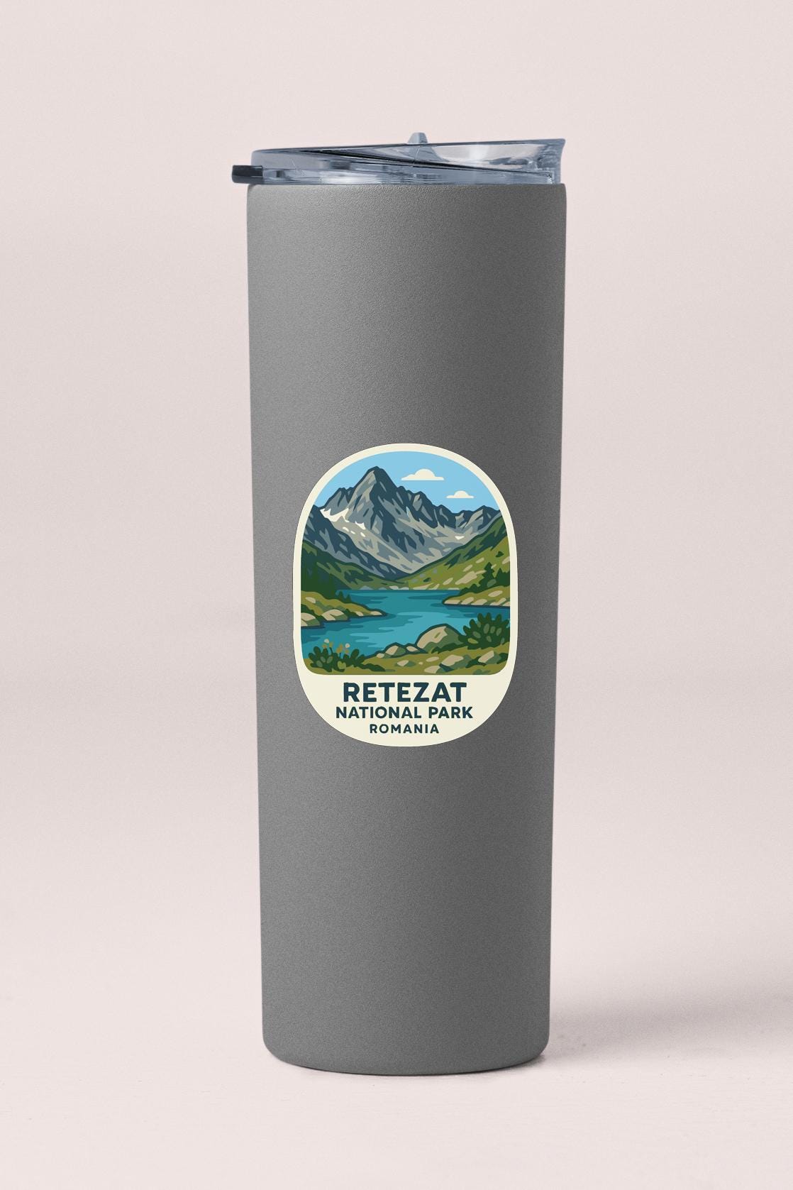 A gray insulated tumbler with a sticker depicting a scenic mountain landscape and the text "RETEZAT NATIONAL PARK ROMANIA".