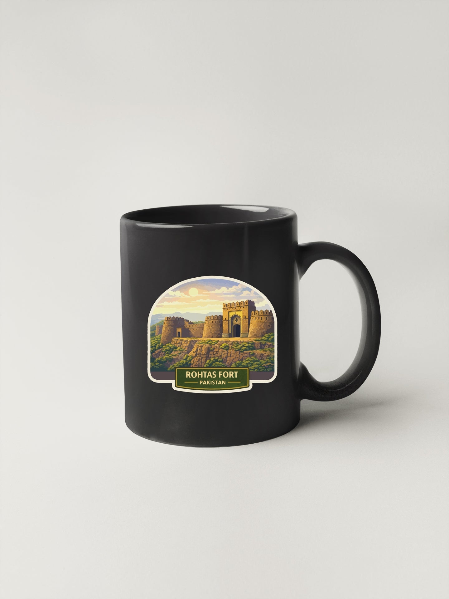 A black coffee mug with a sticker depicting the Rontas Fort in Pakistan.