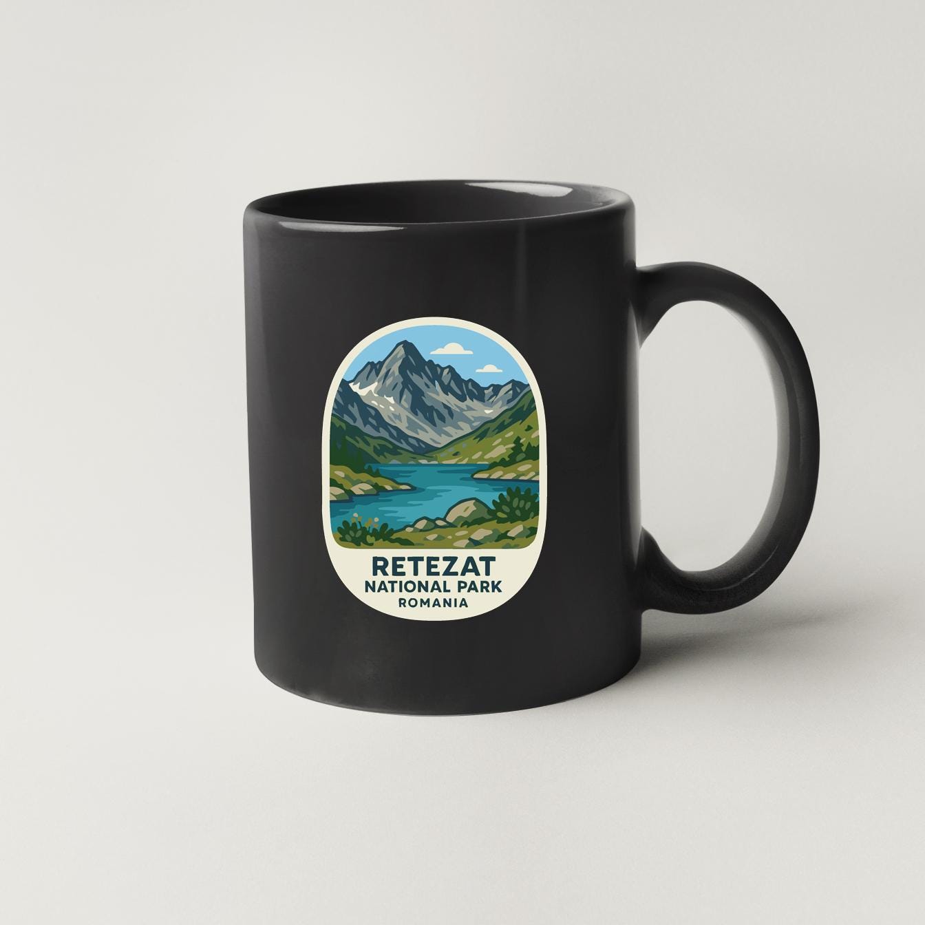 A black coffee mug with a circular design featuring a mountain landscape and a lake, along with the text "RETEZAT NATIONAL PARK ROMANIA".