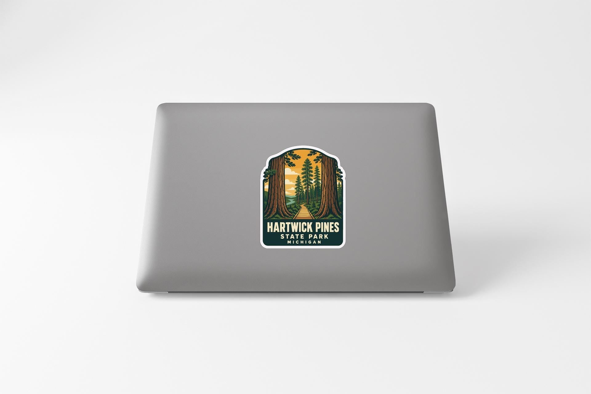 A sticker on the back of a laptop, depicting a scenic forest landscape with tall trees and a path leading through the trees.