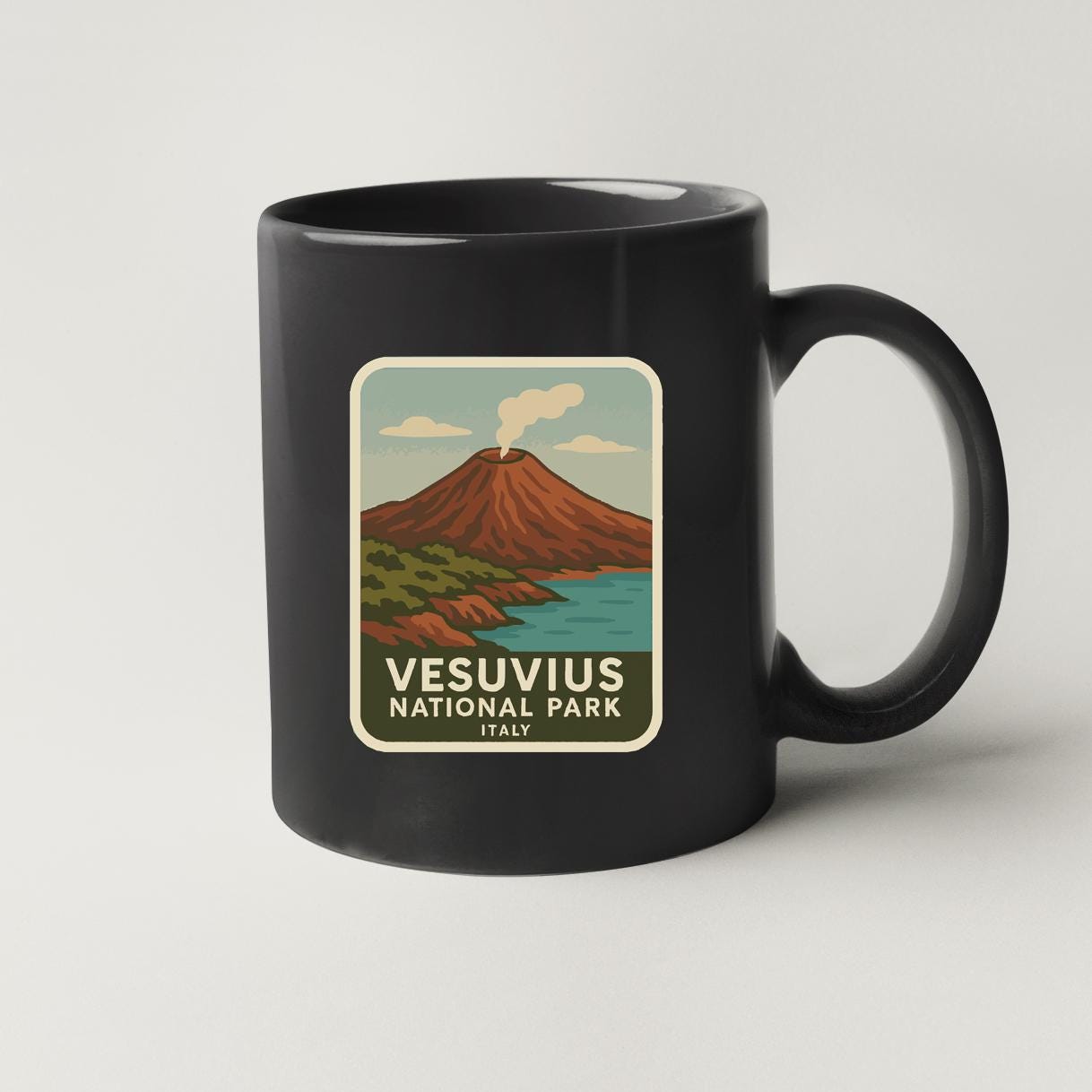 A black coffee mug with a sticker depicting a scenic landscape featuring a volcano and a body of water.