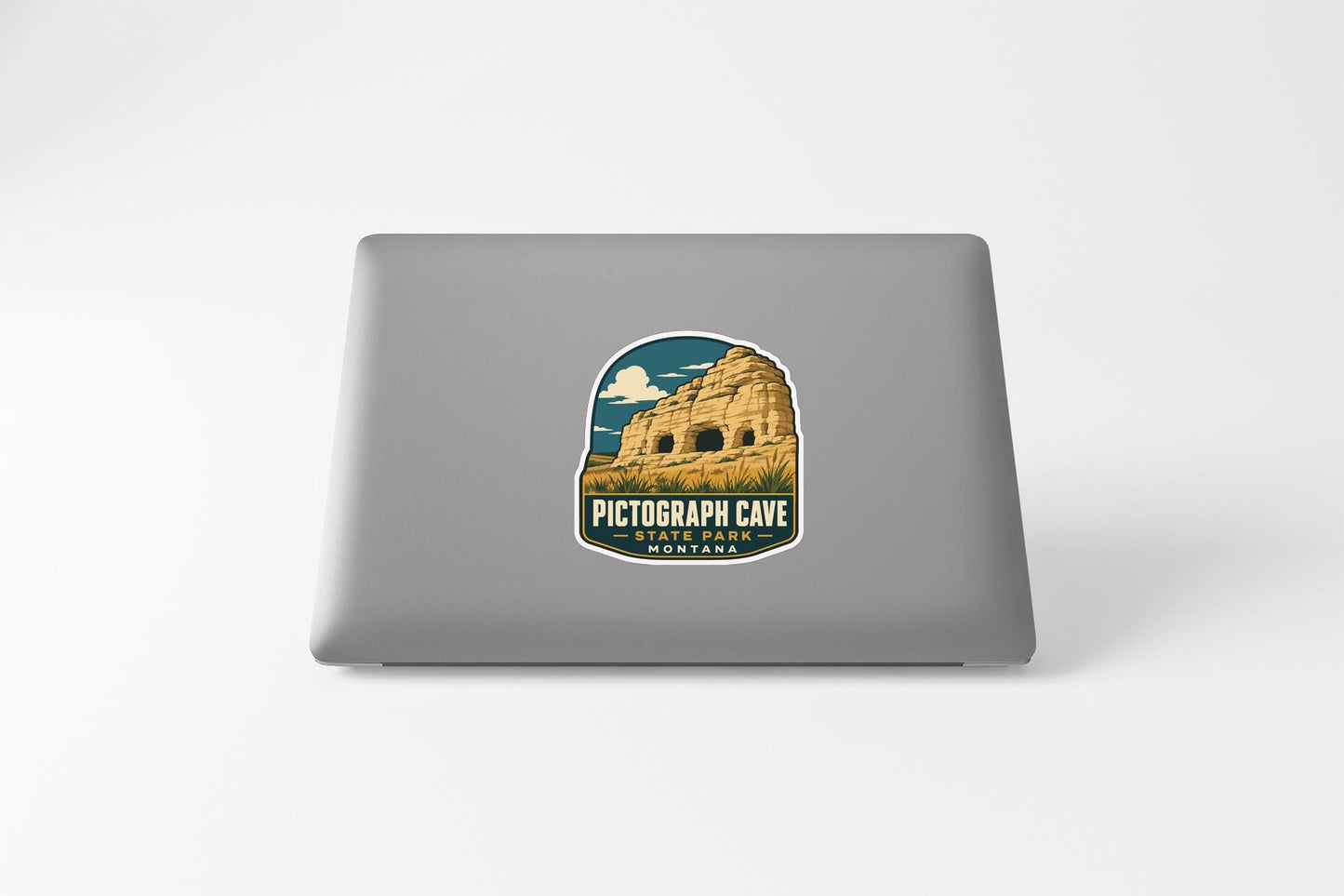 a sticker on a laptop that depicts a cave, with the text "PICTOGRAPH CAVE" and "STARRING MOUNTAINS" printed on it.