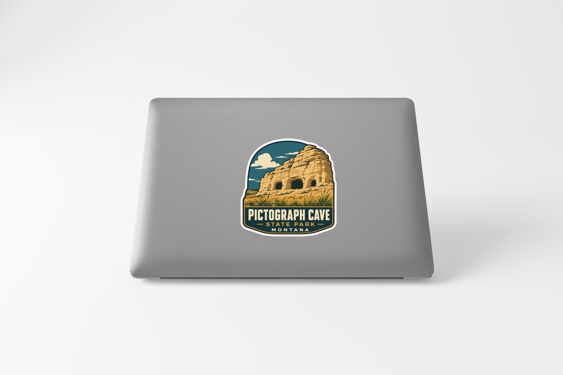 a sticker on a laptop that depicts a cave, with the text "PICTOGRAPH CAVE" and "STARRING MOUNTAINS" printed on it.