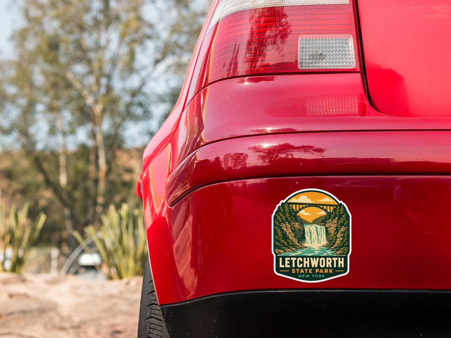the rear end of a red car with a sticker on the back window that says "LECHWORTH STATE PARK NEW YORK".