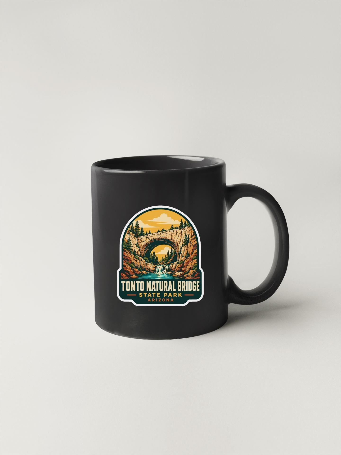 A black coffee mug with a graphic design depicting the Tonto Natural Bridge in Arizona.