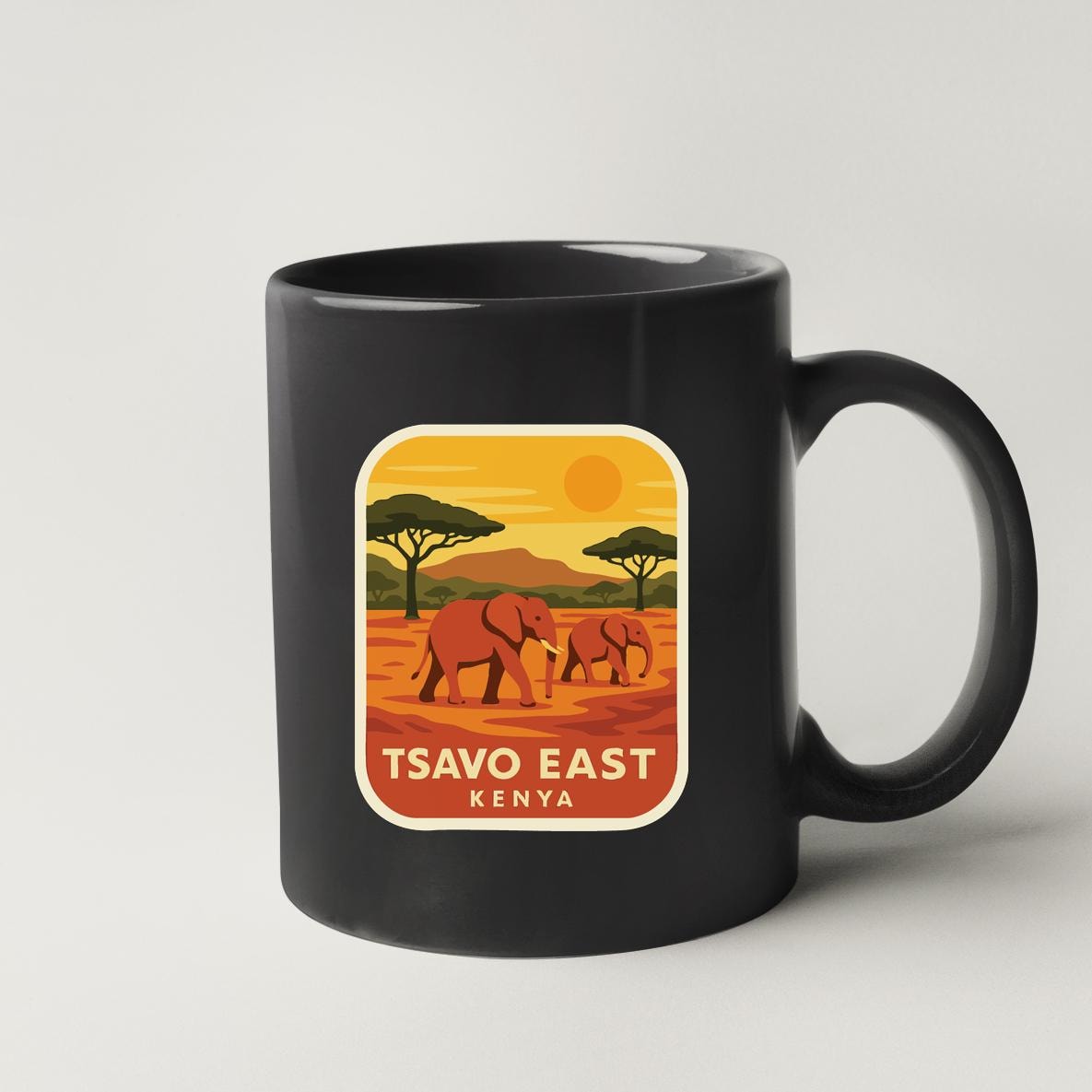 A black coffee mug with a sticker depicting two elephants walking in a savanna landscape with a sunset in the background.
