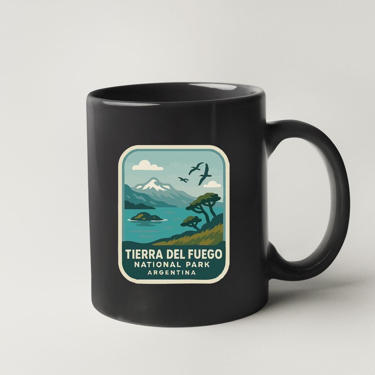 A black coffee mug with a graphic design depicting a scenic landscape with mountains, a lake, and birds flying in the sky.