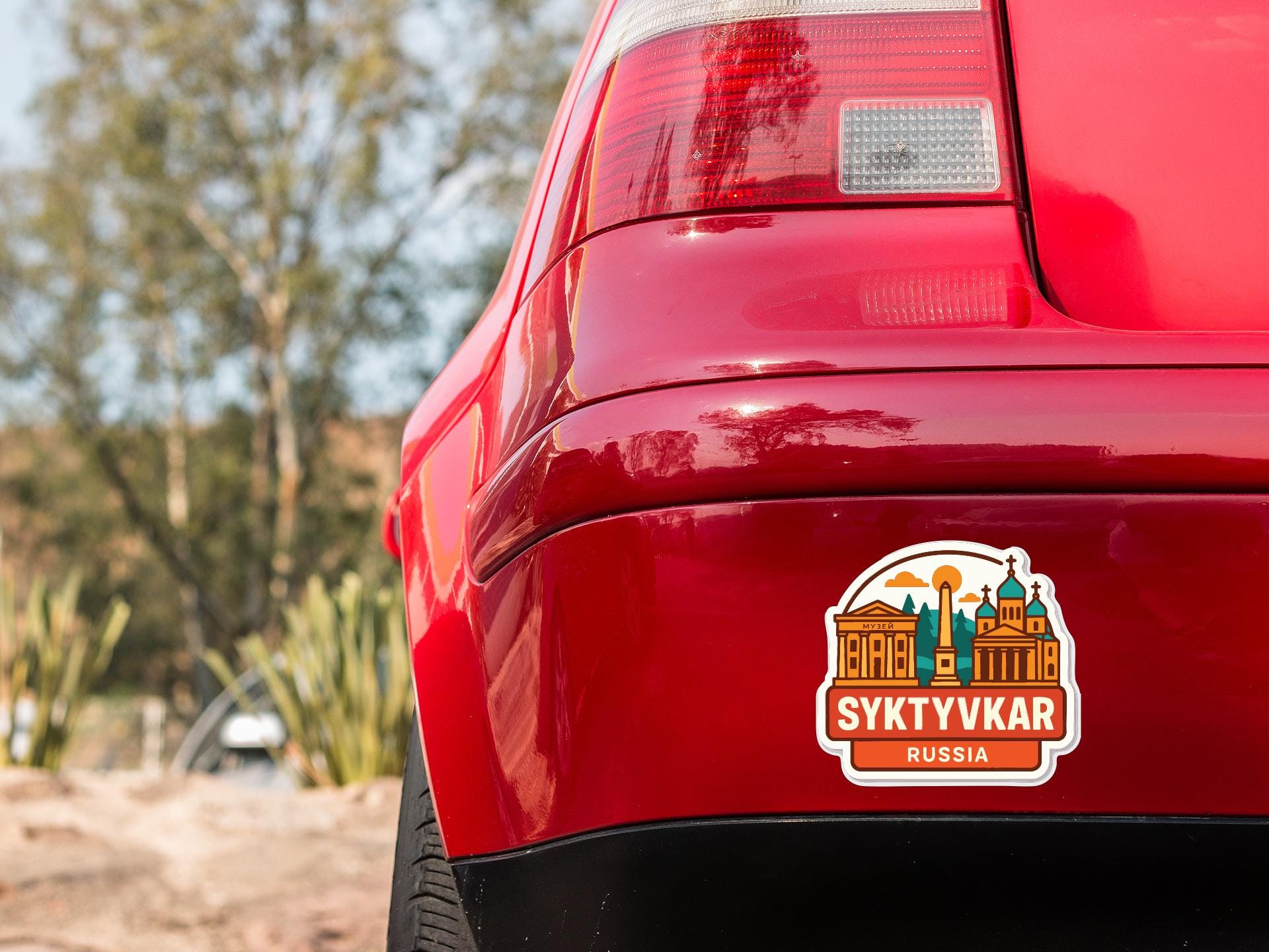 the rear end of a red car with a sticker on the back window that displays the text "SYKYVKAR RUSSIA".