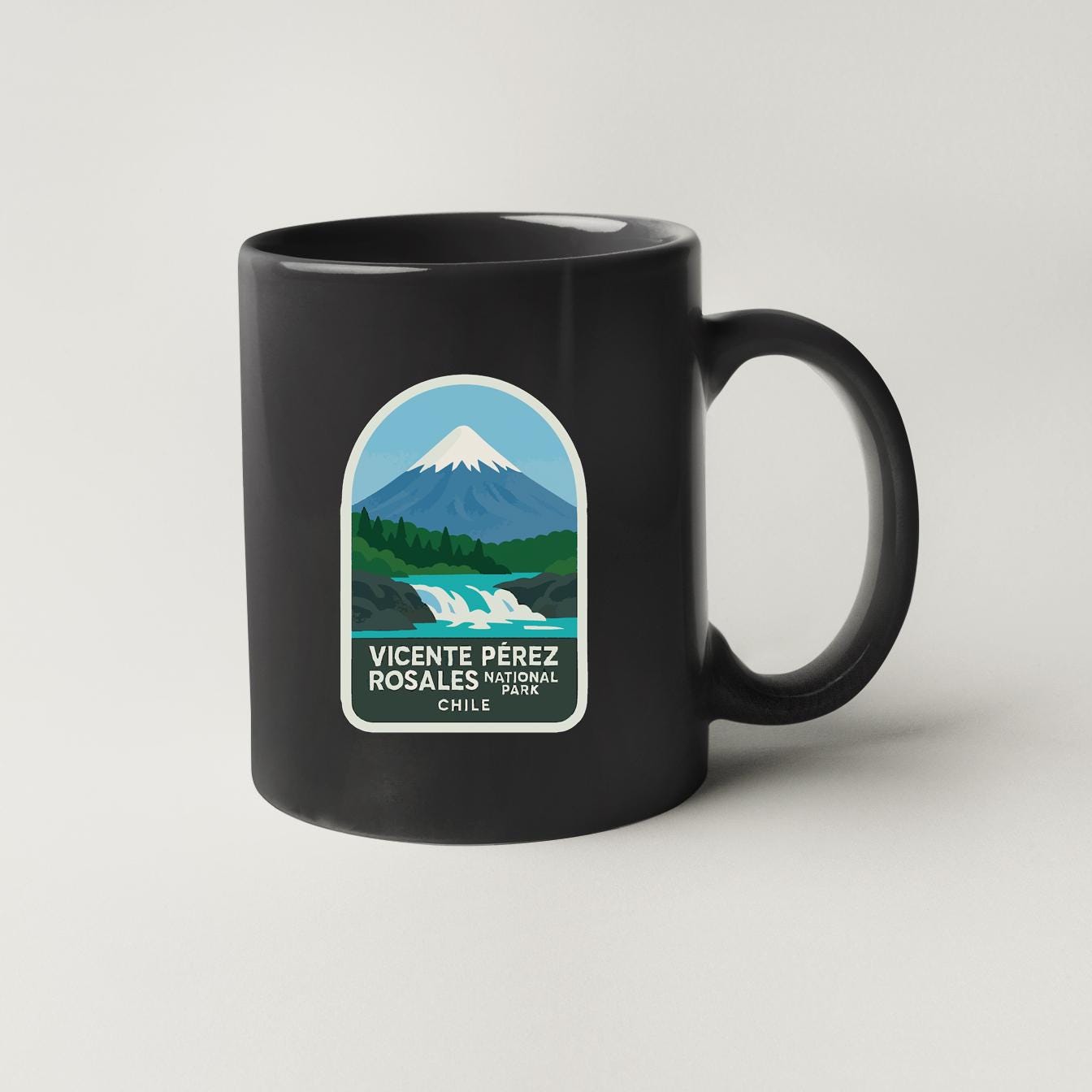 A black coffee mug with a graphic design depicting a mountain landscape, including a snow-capped peak, a waterfall, and a forested area.