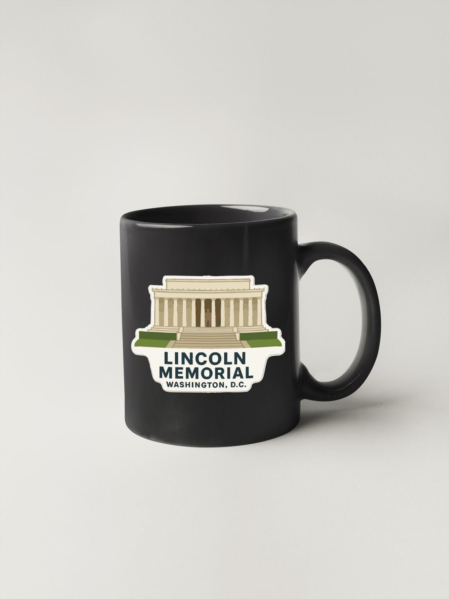 A black coffee mug with a sticker depicting the Lincoln Memorial in Washington, D.C.
