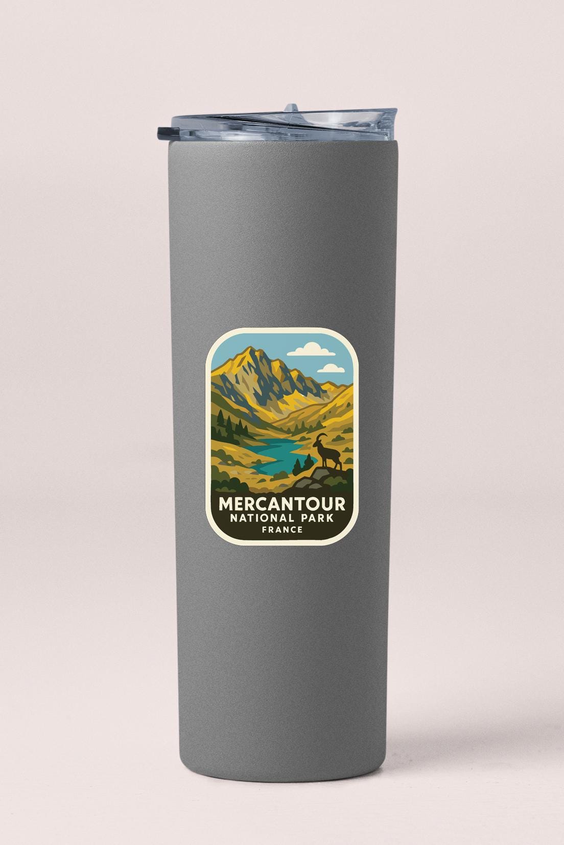 A gray tumbler with a sticker depicting a mountain landscape and the text "MERCANTOUR NATIONAL PARK FRANCE".