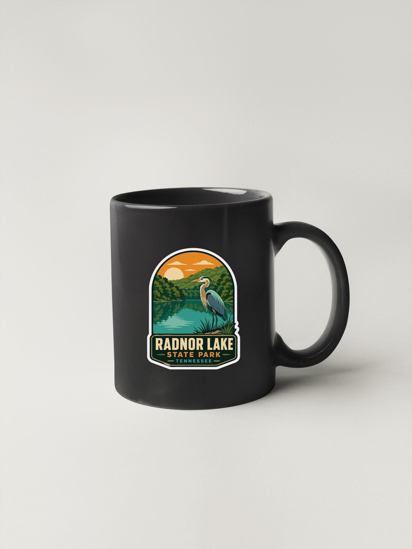 A black coffee mug with a sticker depicting a scenic landscape featuring a lake, mountains, and a bird.