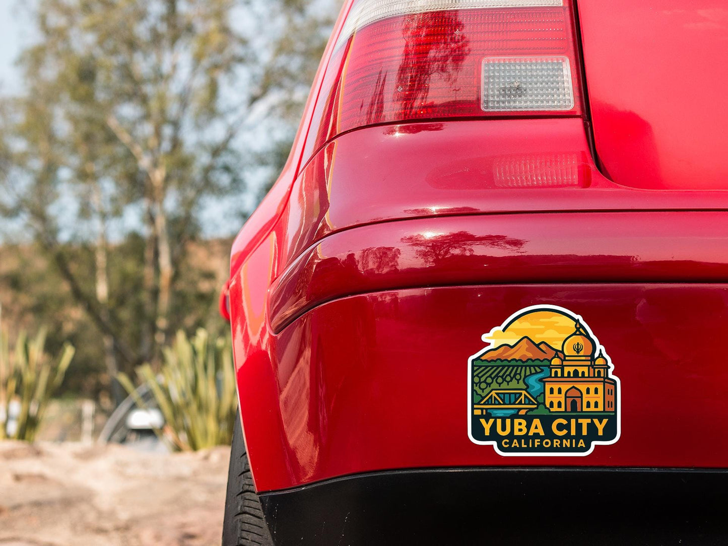 the rear end of a red car with a sticker on the trunk that says "Yuba City, California".