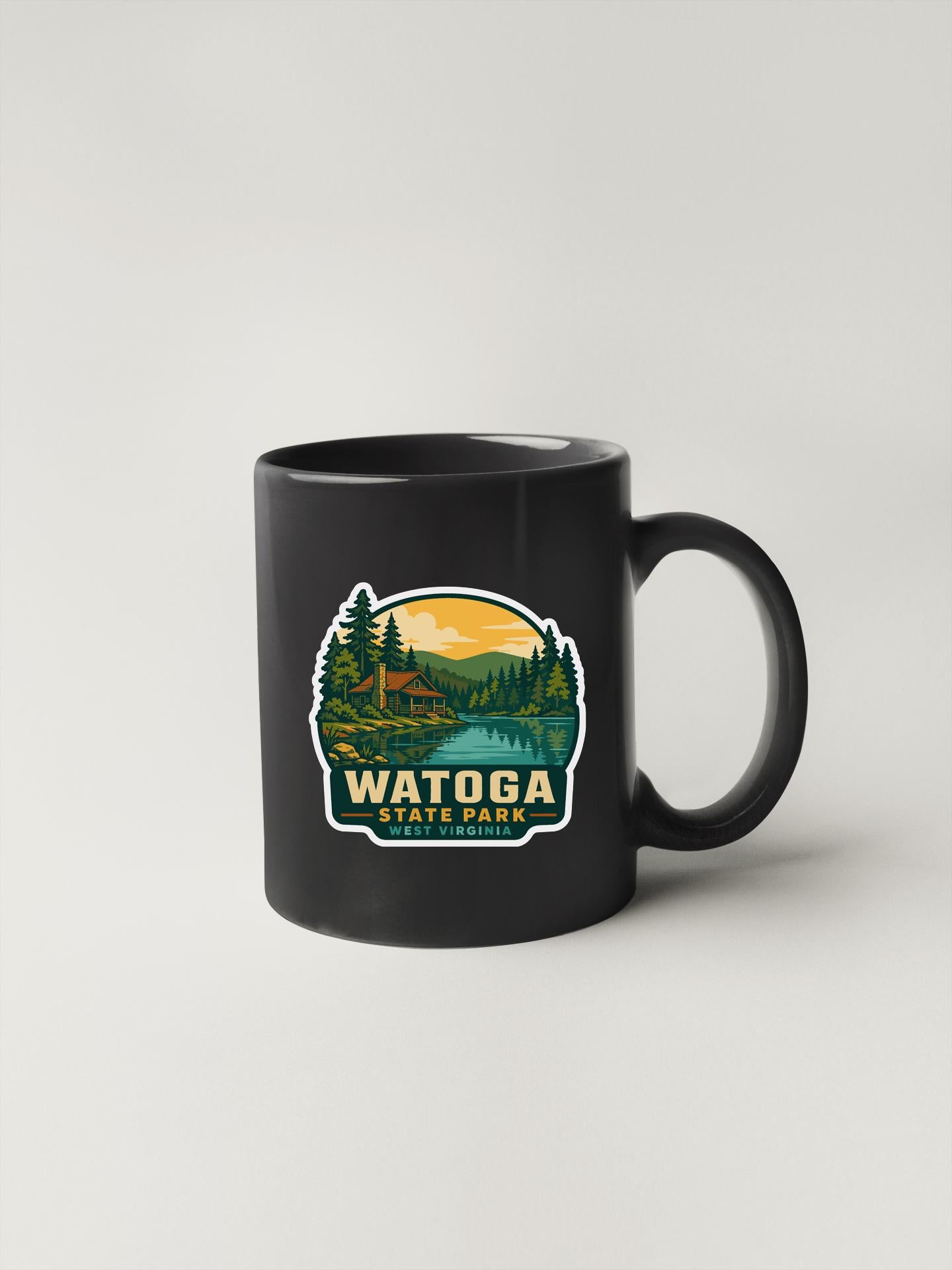 A black coffee mug with a sticker depicting a scenic landscape featuring a cabin and trees, along with the text "WATOGA STATE PARK" printed on it.