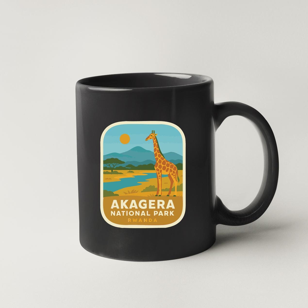 A black coffee mug with a label that features an illustration of a giraffe in a natural landscape, along with the text "AKAGERA NATIONAL PARK" and " RWANDA".