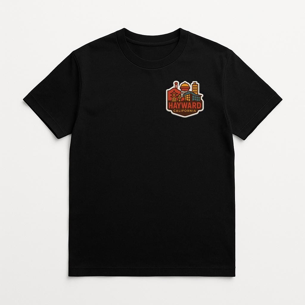 A black t-shirt with a colorful graphic design on the front, depicting a city skyline with buildings and a prominent "HAYWARD" logo.