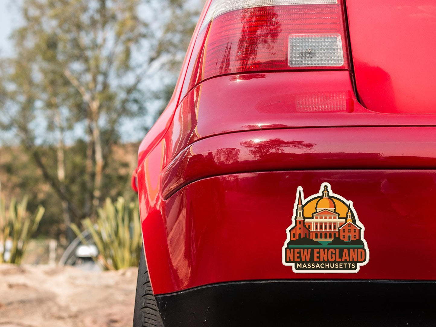 the rear end of a red car with a New England Massachusetts license plate sticker on the trunk.