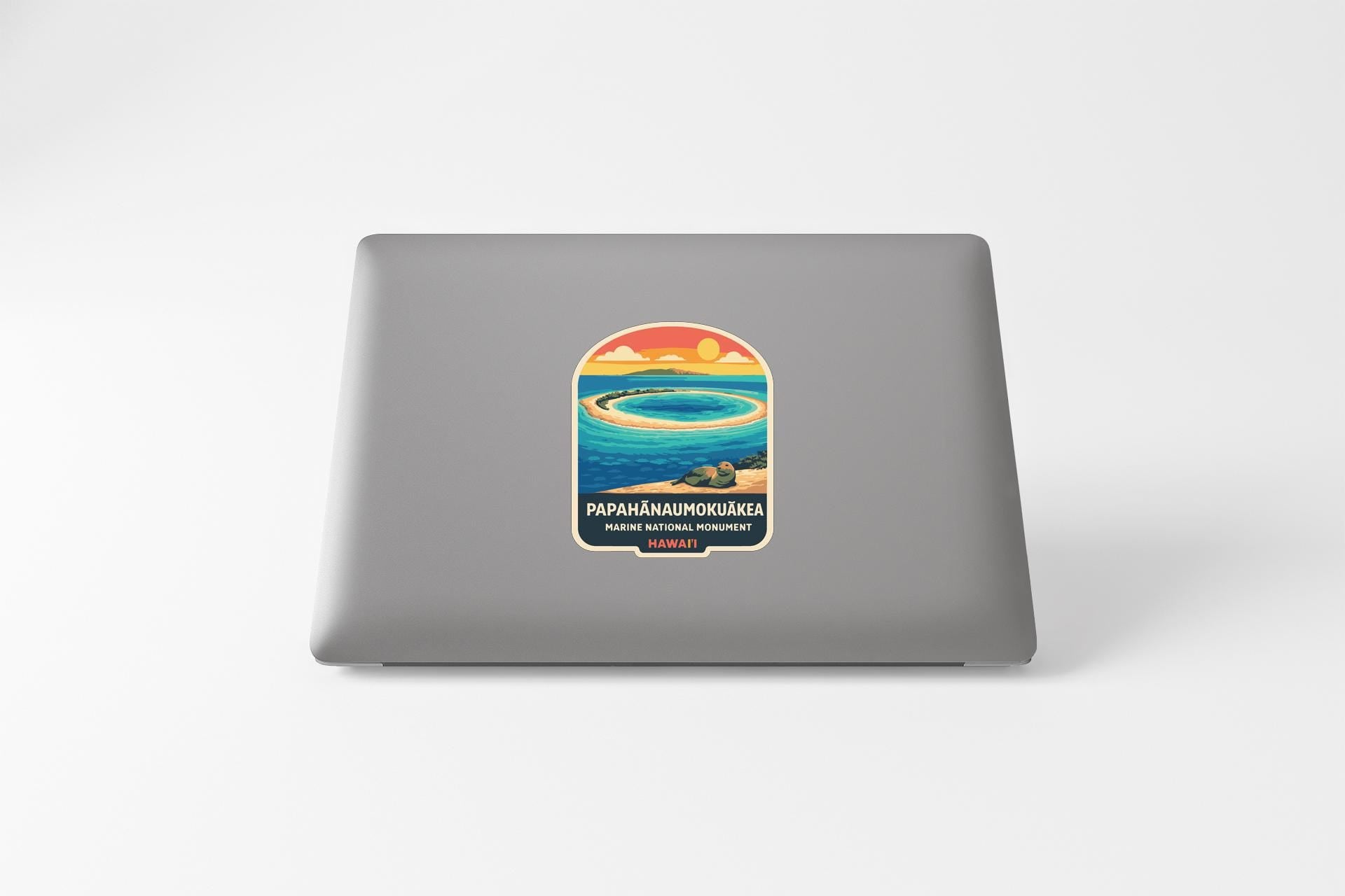 A sticker on the back of a laptop, depicting a tropical island with a sunset over the ocean.