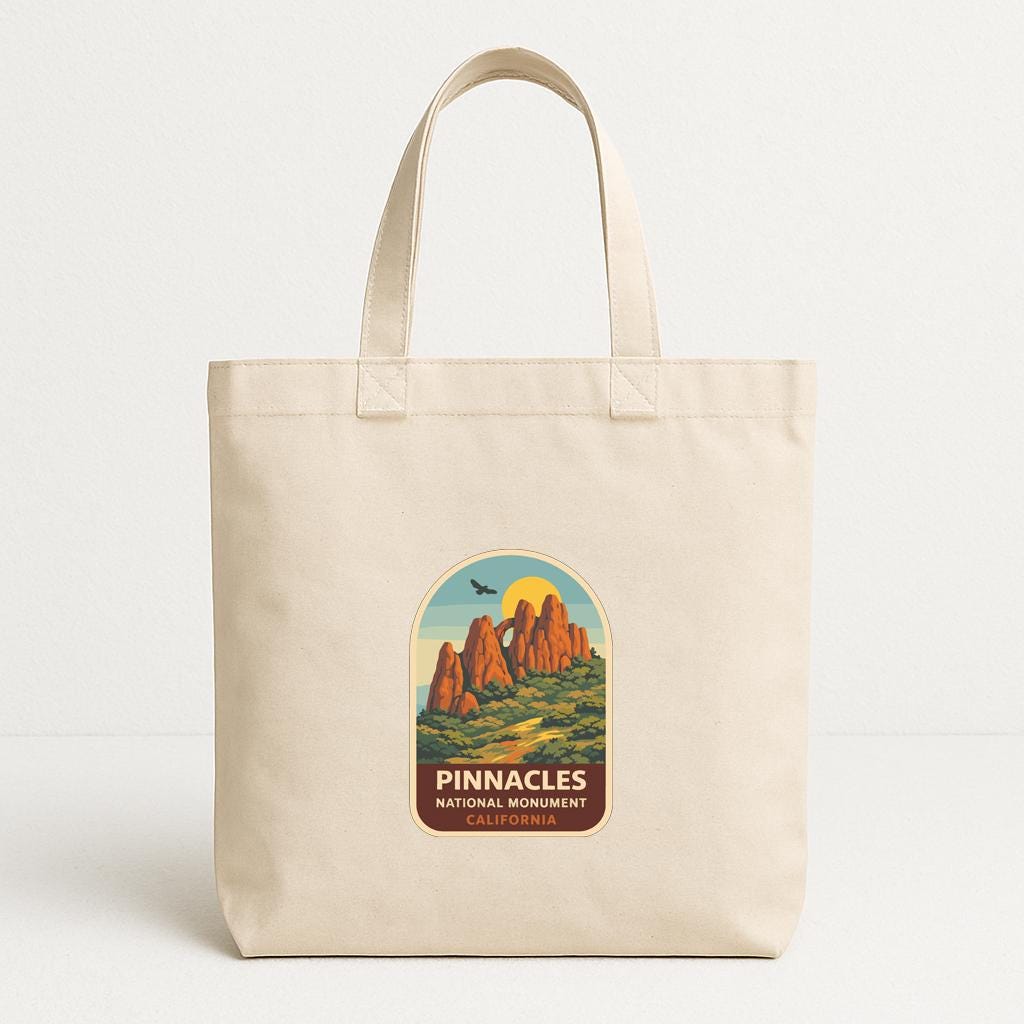 A beige tote bag with a graphic design featuring a mountain range and the text "PINNACLES NATIONAL MONUMENT CALIFORNIA" printed on it.