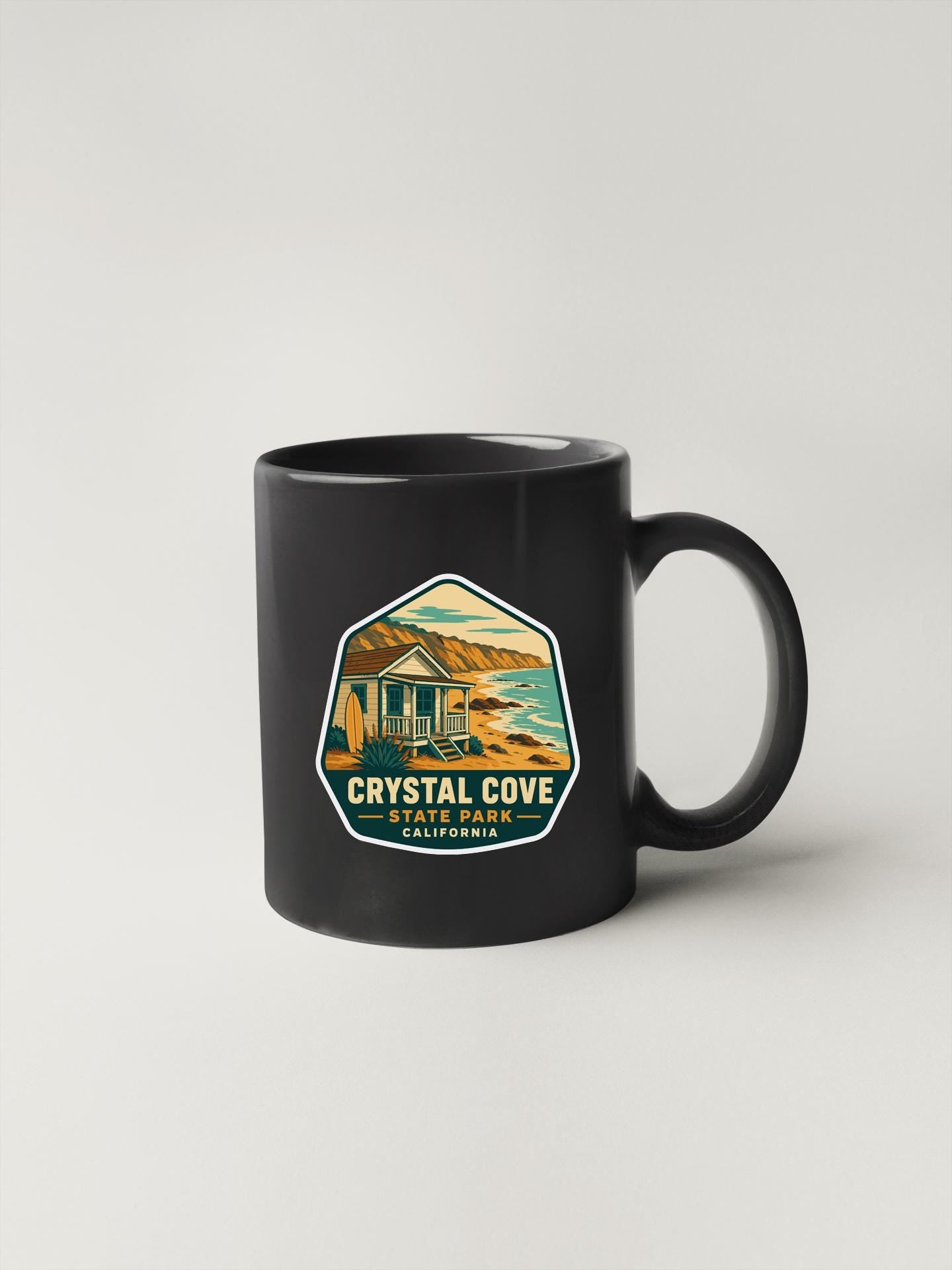A black coffee mug with a label that says "CRYSTAL COVE STATE PARK CALIFORNIA".