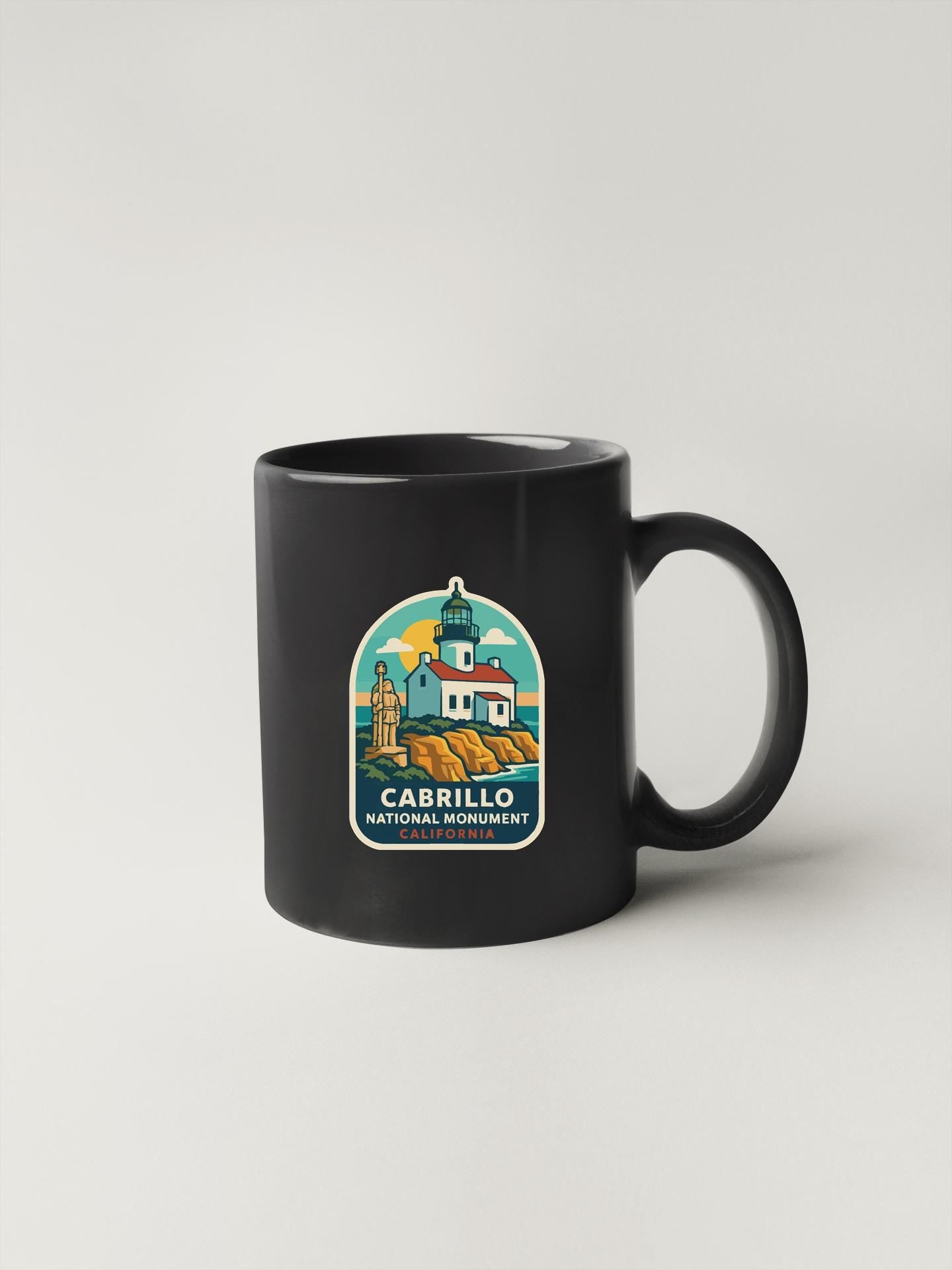A black coffee mug with a colorful illustration of a lighthouse and a building, along with the text "CABRILLO NATIONAL MONUMENT" printed on it.