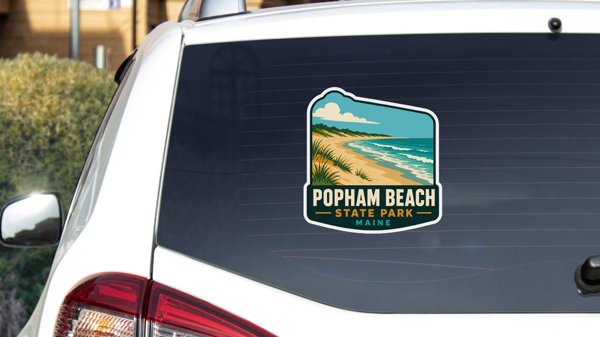 A sticker on the rear window of a white vehicle, depicting a scenic beach landscape with a sandy beach, ocean waves, and a cloudy sky.