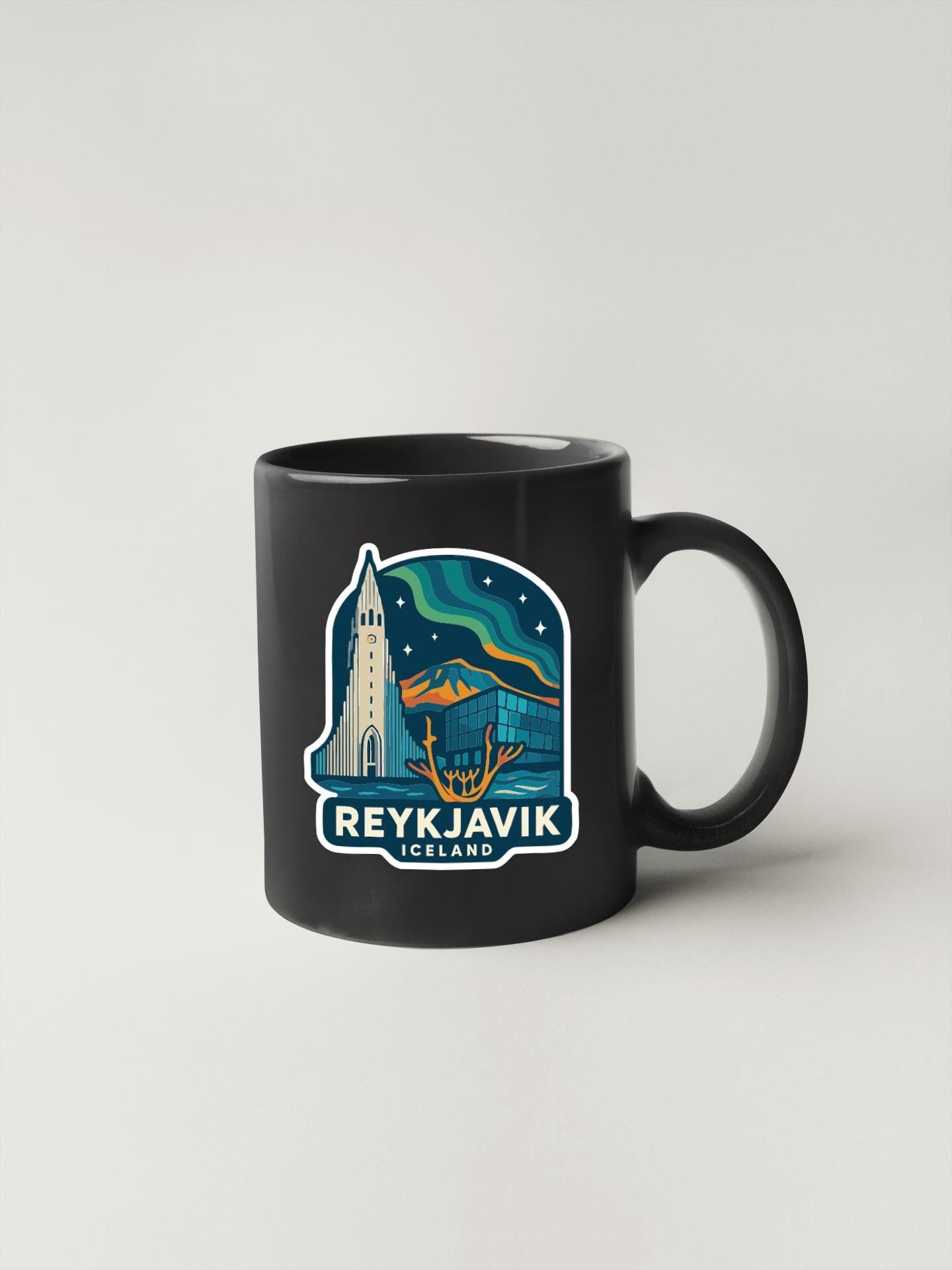 A black coffee mug with a colorful illustration of Reykjavik, Iceland, featuring a castle, mountains, and the Northern Lights.