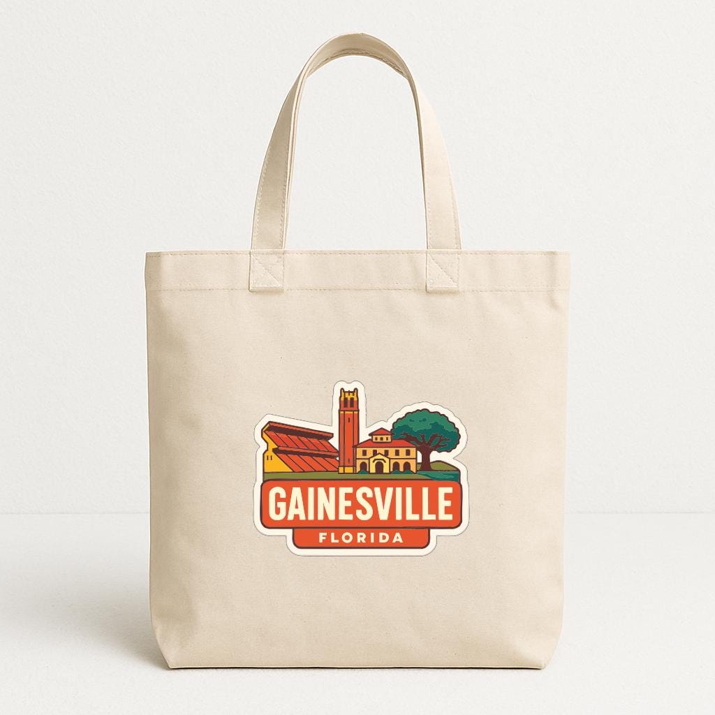 A beige tote bag with a graphic design depicting a cityscape and the text "GAINESVILLE FLORIDA" printed on it.