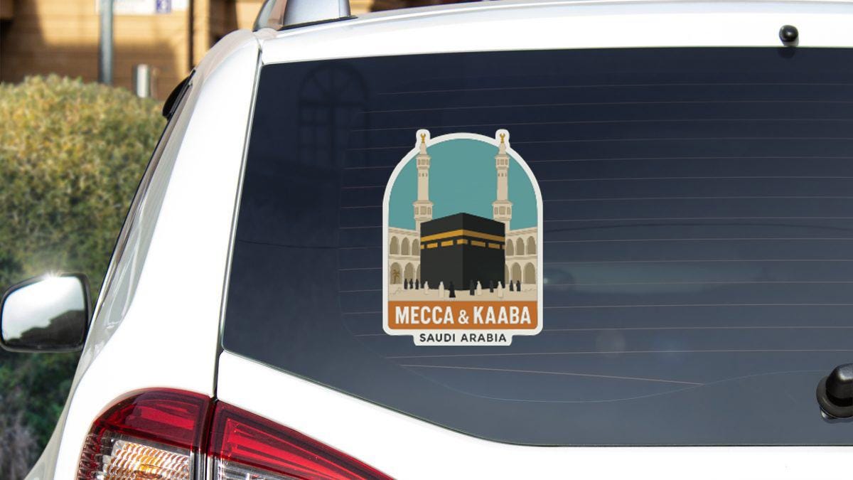 A sticker on the rear window of a car, depicting the Kaaba and Mecca, with the text "MECCA & KABA SAUDI ARABIA" below the sticker.