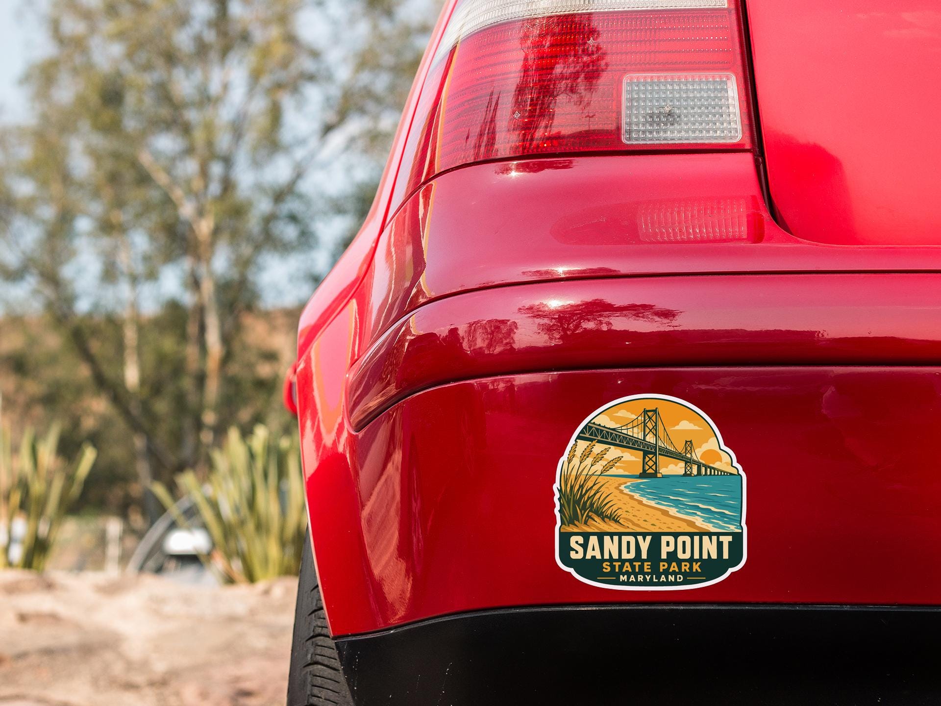 the rear end of a red car with a sticker on the back window that says "Sandy Point State Park Maryland".