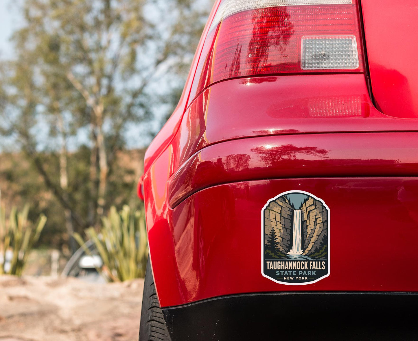 the rear end of a red car with a taichnock falls sticker on the trunk.