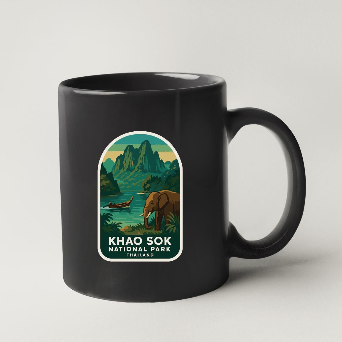 A black coffee mug with a sticker depicting a scenic landscape of mountains, water, and an elephant.