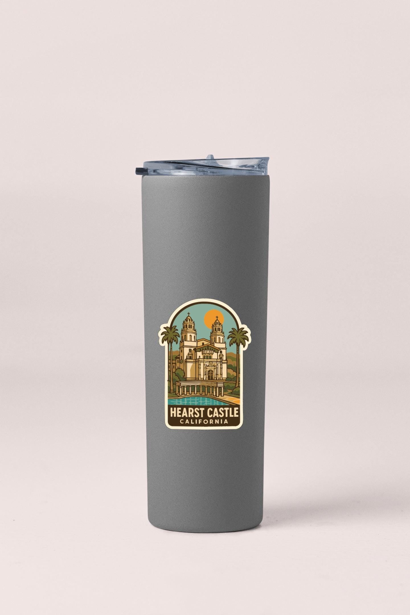 A gray insulated tumbler with a sticker depicting the Heast Castle in California.