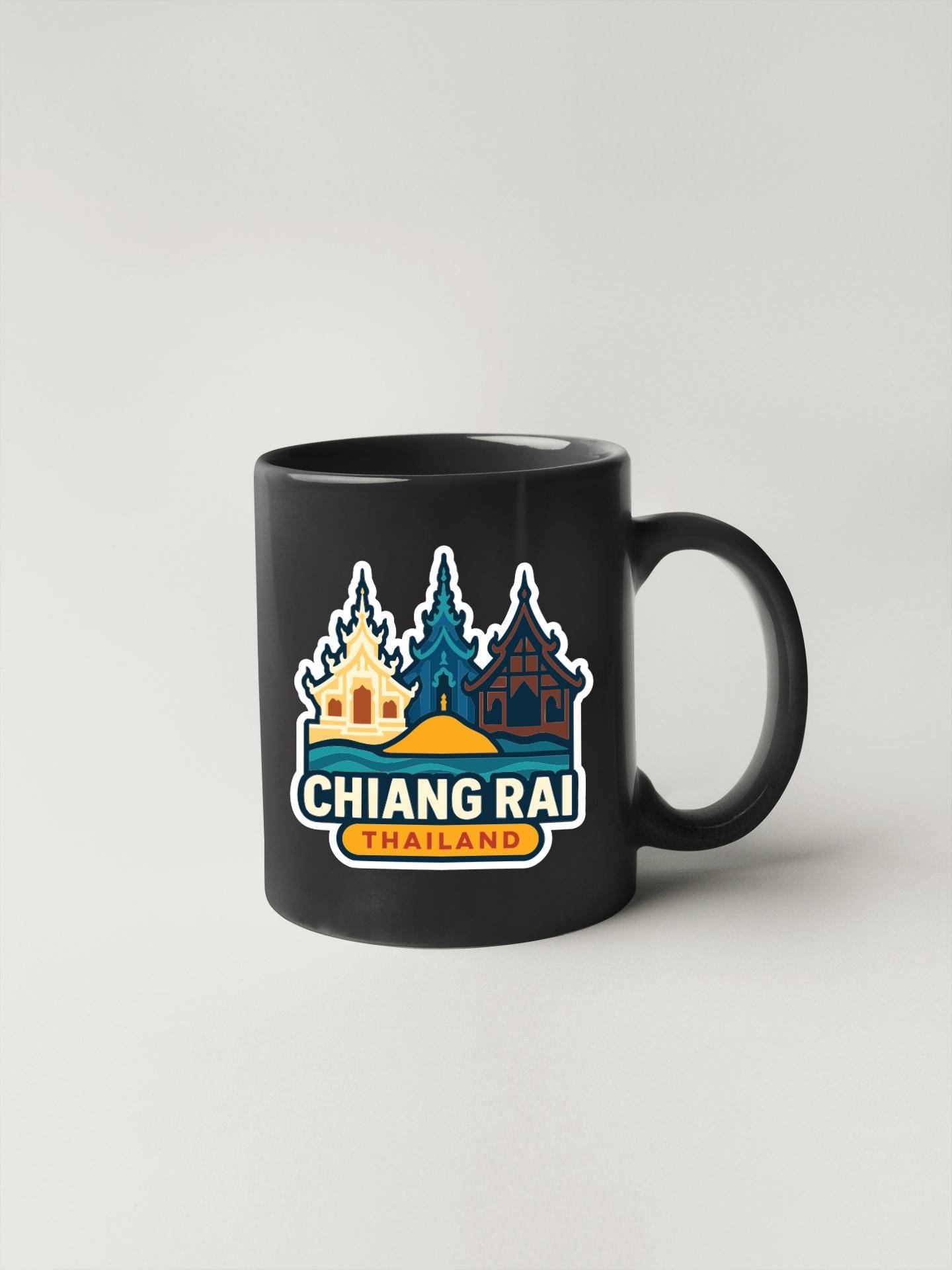 A black coffee mug with a colorful graphic design featuring three stylized buildings and the text "CHIANG RAI THAILAND".