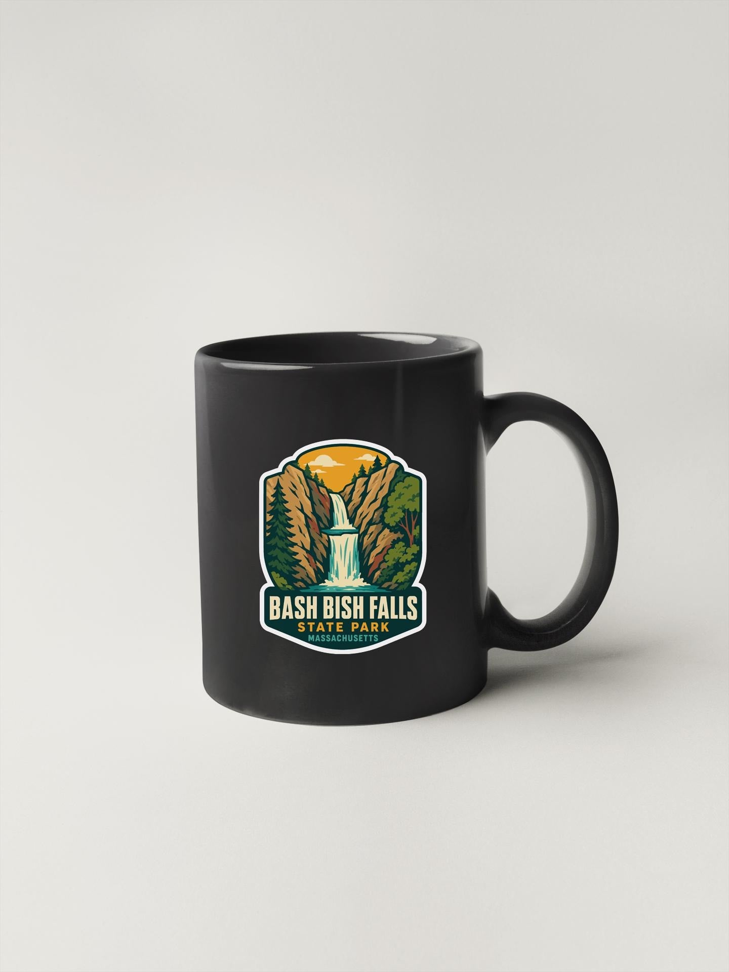 A black coffee mug with a graphic design depicting a waterfall and mountains, along with the text "Bash Bish Falls State Park, Massachusetts".