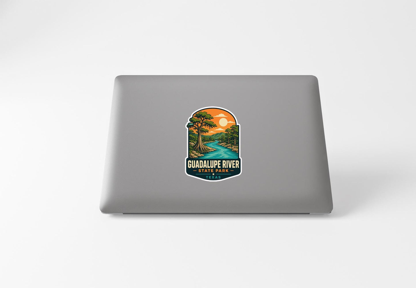 a sticker on the back of a laptop that depicts a scenic landscape with a river and a sunset.
