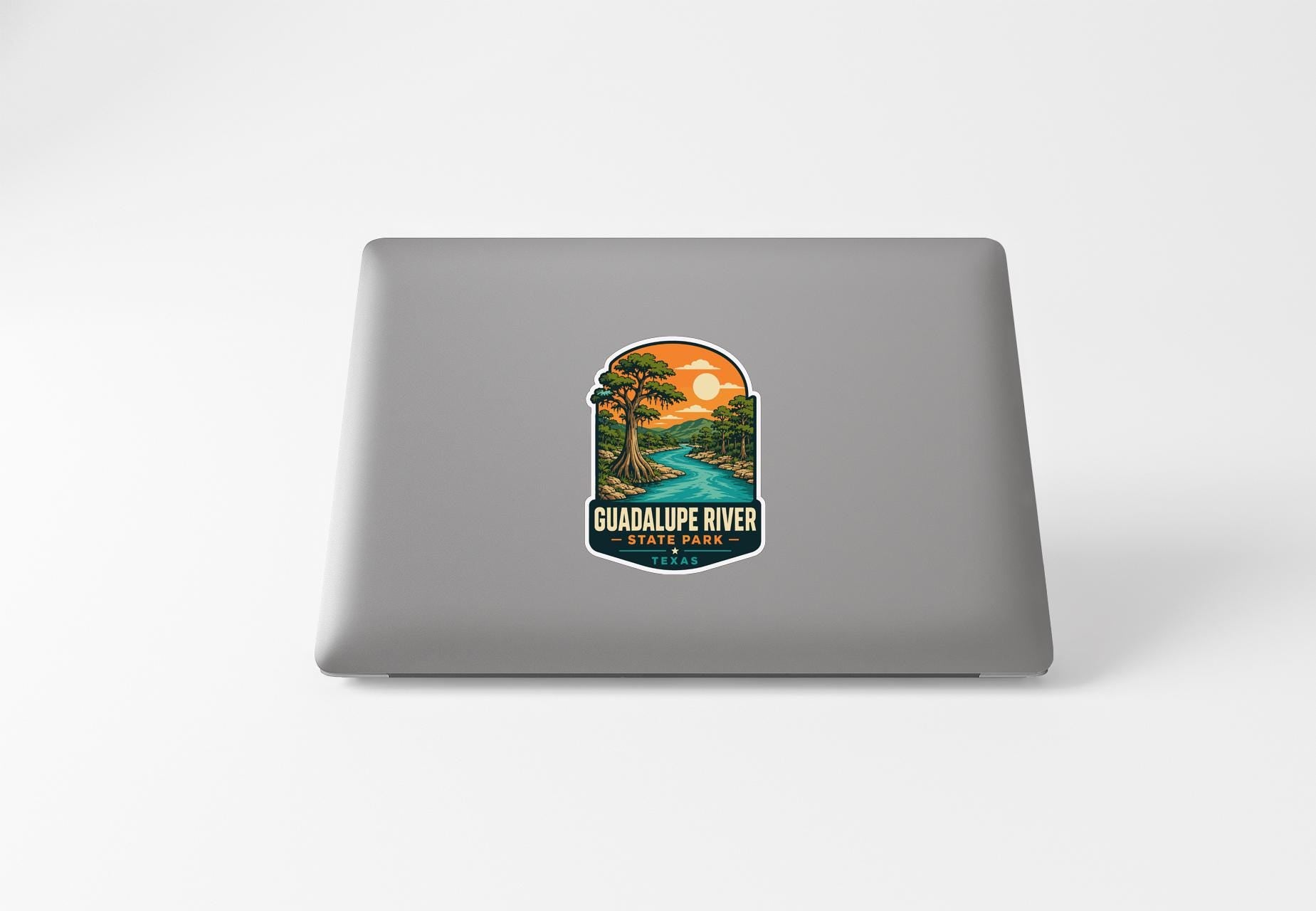 a sticker on the back of a laptop that depicts a scenic landscape with a river and a sunset.