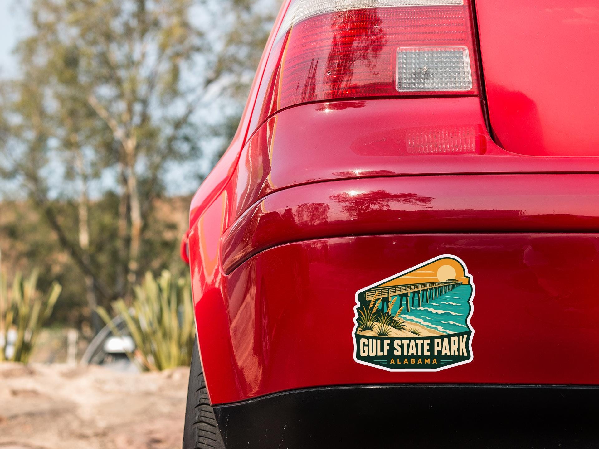 the rear end of a red car with a sticker on the back window that says "Gulf State Park Alabama".