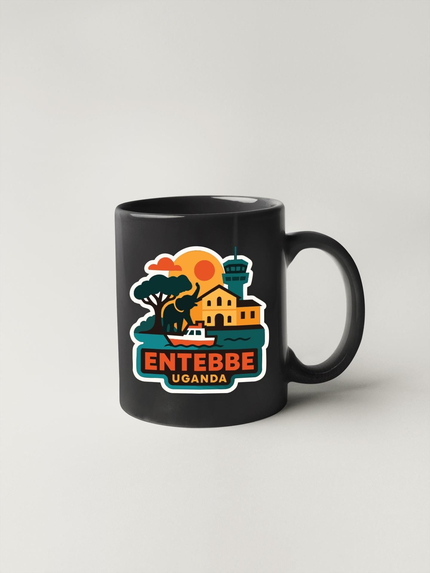 A black coffee mug with a colorful illustration of a town and a sunset, along with the text "ENTEBBE UGANDA" printed on it.