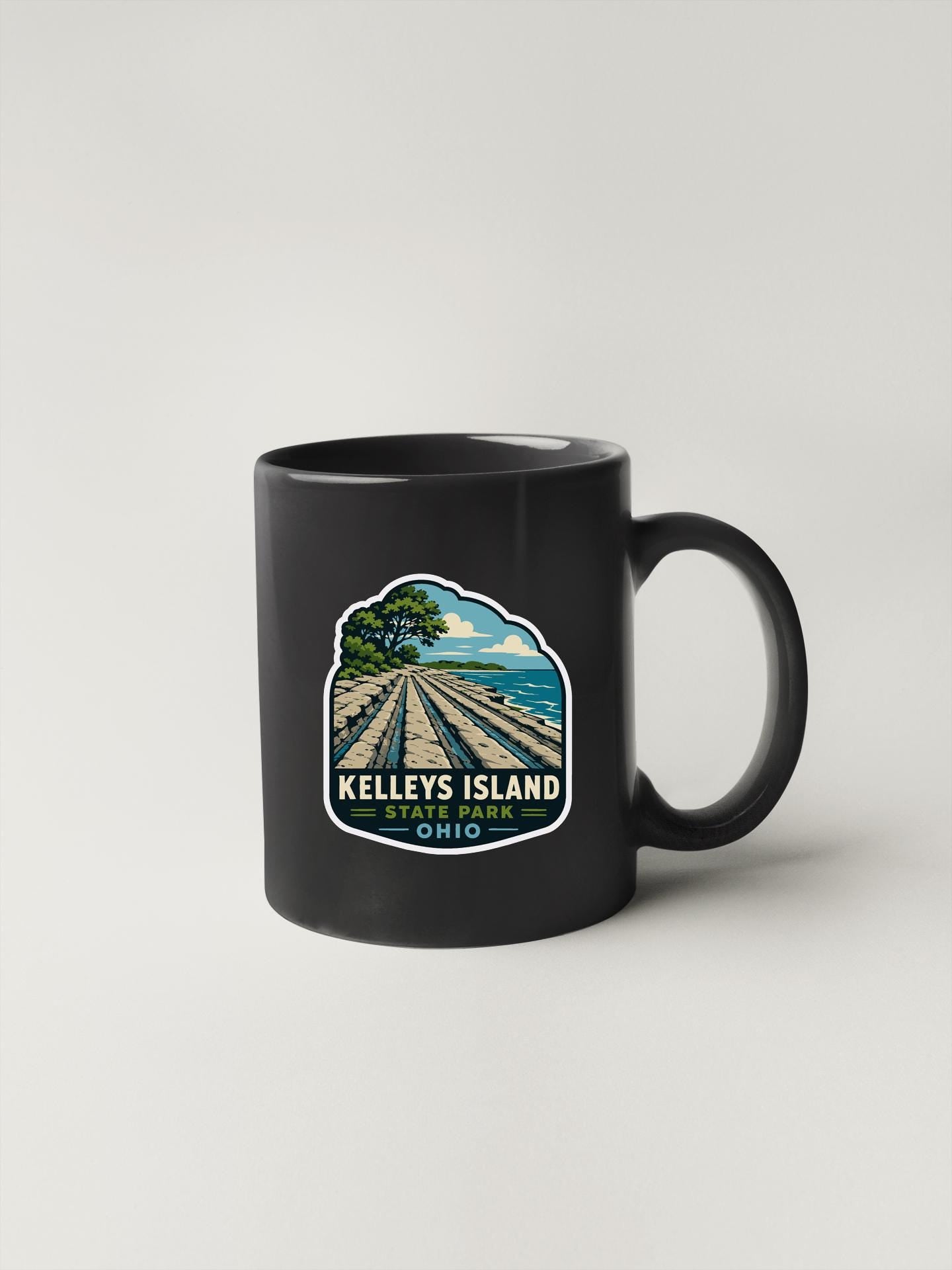 A black coffee mug with a sticker depicting a scenic view of Kelley's Island, Ohio.