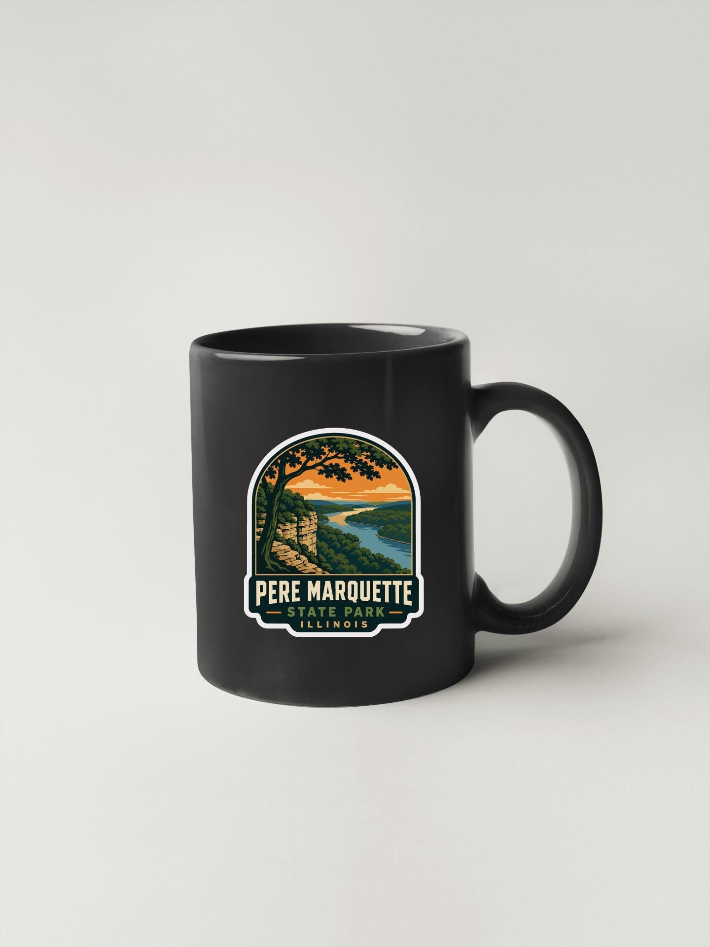 A black coffee mug with a graphic design depicting a scenic landscape, including a river, mountains, and a sunset.